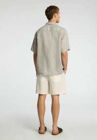 Koszula z krótkim rękawem w jasnoszarym kolorze z lnu o luźnym kroju, zestawiona z szortami w kolorze kremowym. Materiał nie odbijający światła, casualowy design.