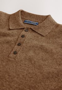 Braunes, geripptes Strick-Poloshirt mit Kragen, ausgestattet mit vier dunklen Knöpfen und einem Etikett mit blauer und goldener Schrift. Weicher Stoff, schlichtes Design.