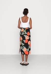 Saia midi floral com fundo preto, apresentando grandes rosas corais e pequenas flores azuis. Combinada com uma blusa de alças branca e sandálias chunky.