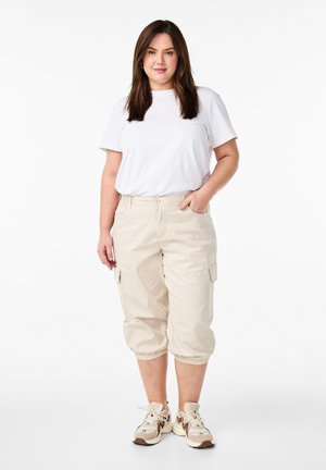 Beige cargo pants with elastic cuffs and side pockets, paired with a fitted white t-shirt and light-colored athletic shoes.
