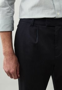 Fekete szabott nadrág sima textúrával, elülső pliszékkel és karcsú derekú fazonnal. Fénykék és fehér csíkos inggel párosítva.