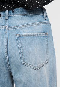 Οπίσθια όψη ατόμου που φοράει ανοιχτό μπλε τζιν με πίσω τσέπη και μαύρο τοπ με πουά