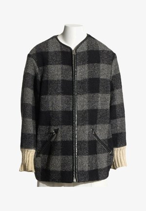 Veste zippée à carreaux noirs et gris avec des poignets en côte couleur crème et deux poches avant zippées sur un buste de mannequin blanc.