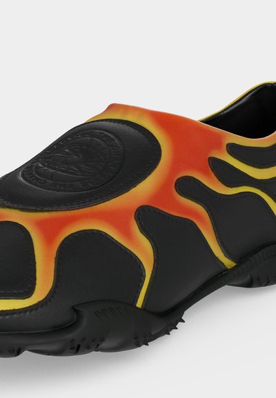 Slip-on αθλητικό παπούτσι με μαύρη βάση και φλόγες σε κίτρινο και πορτοκαλί, με ανεβασμένο κυκλικό λογότυπο στο μπροστινό μέρος.