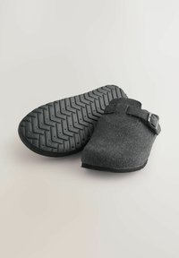 Graue Filzclogs mit einer schwarzen Gummisohle, die ein Fischgrätmuster aufweist, verstellbarem Riemen mit einer Metallschnalle und offenem Rücken-Design.