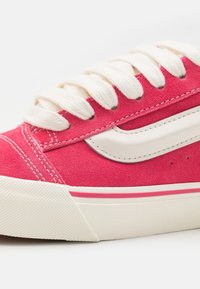 Baskets en daim rose avec bande blanche, lacets épais blancs et semelle blanche texturée avec bande accent rose.