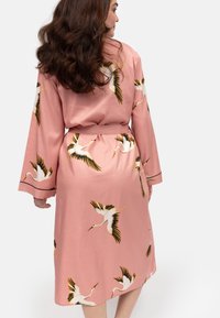 Różowy szlafrok w stylu kimona z paskiem w talii, ozdobiony białymi żurawiami i czarnymi akcentami. Długie rękawy i gładka faktura tkaniny.