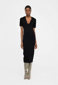 Czarna, dopasowana sukienka midi z głębokim dekoltem w serek, krótkimi rękawami i fakturowanymi detalami na ramionach. Noszona z wysokimi botkami za kolano w wężowy wzór.