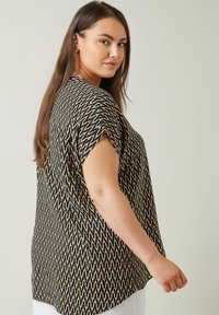 Top de patrón negro y dorado con mangas cortas, corte relajado y un sutil diseño en forma de chevrón. Tejido texturizado con un acabado suave.