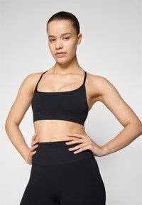 Sujeción deportiva negra con tirantes finos, con una textura suave y un ajuste ceñido. Diseño simple sin patrones ni adornos.