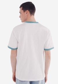 Weißes T-Shirt mit türkisen Akzenten am Kragen und an den Ärmeln. Klassisches Design mit kurzen Ärmeln und einer lockeren Passform, aus weichem Stoff gefertigt.
