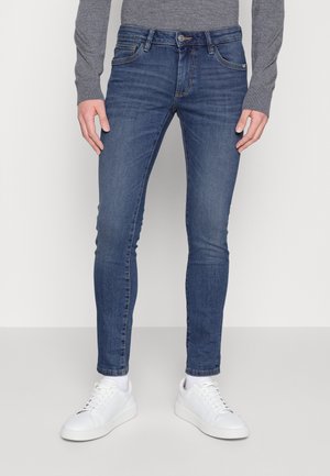Jeans azules de corte slim hechos de denim con un diseño clásico de cinco bolsillos. Llevados con zapatillas blancas, presentan una silueta de pierna ajustada.