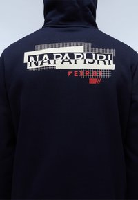 Navy hoodie met het "NAPAPIJRI" logo in crème en rood, met ruitpatronen en grafische accenten op de achterkant, gemaakt van zachte stof.