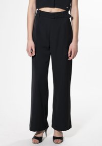 Zwarte wijde broek van een gladde stof, met een ceintuur om de taille en zijnaad. Gecombineerd met zwarte open-toe hakken.