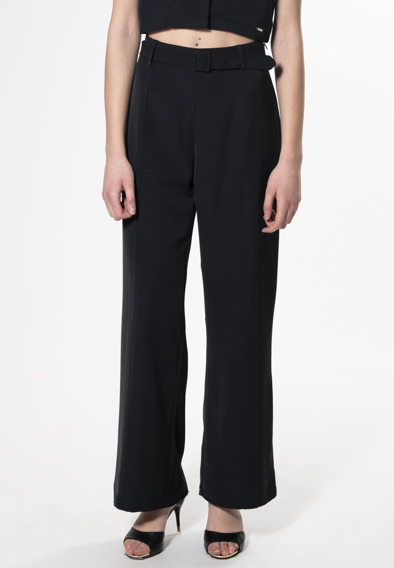 Zwarte wijde broek van een gladde stof, met een ceintuur om de taille en zijnaad. Gecombineerd met zwarte open-toe hakken.