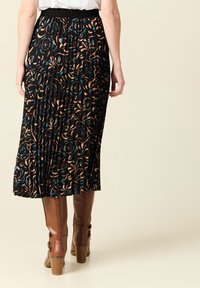 Zwarte geplooide rok met een bloemenpatroon in perzik, teal en bruin. Gekocht met bruine kniehoge laarzen met een decoratieve gesp.