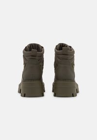 Un par de botas tobilleras verde oliva con suelas gruesas y tiradores, mostradas desde atrás sobre un fondo blanco.