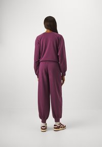 Violetti collegeasu, jossa on löysä yläosa pyöreällä pääntiellä ja joustovyötäröllä varustetut housut, valmistettu pehmeästä kankaasta ja varustettu resoreilla hihansuissa.