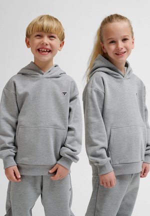 Grijze hoodies van zachte stof, met voorzakken en geribbelde manchetten. Twee kinderen die glimlachen, in bijpassende trainingsbroeken.