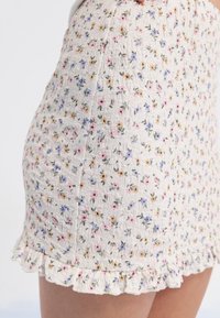 Minifalda floral, tejido blanco texturizado con flores en tonos pastel. Dobladillo con volantes, diseño ajustado, pequeños patrones de flores en rosa, púrpura y amarillo.
