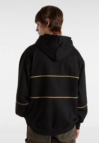 Svart hoodie med snörning i huvan som har gula horisontella ränder. Tjockt material, avslappnad passform, ribbade ärmslut och nederkant.