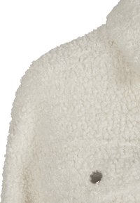Veste polaire blanche texturée avec tissu bouclé et bouton-pression argenté visible au niveau de la poitrine.