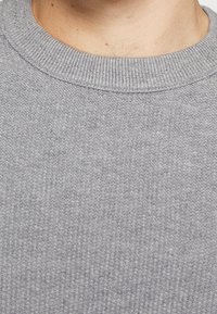 Pull en maille grise avec un col côtelé et un tissu texturé présentant un motif subtil, soulignant une apparence douce et confortable.