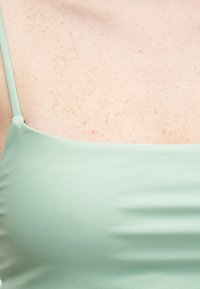 Gros plan sur une peau tachetée et un top fines bretelles vert menthe sur la partie supérieure de la poitrine et de l'épaule d'une personne.