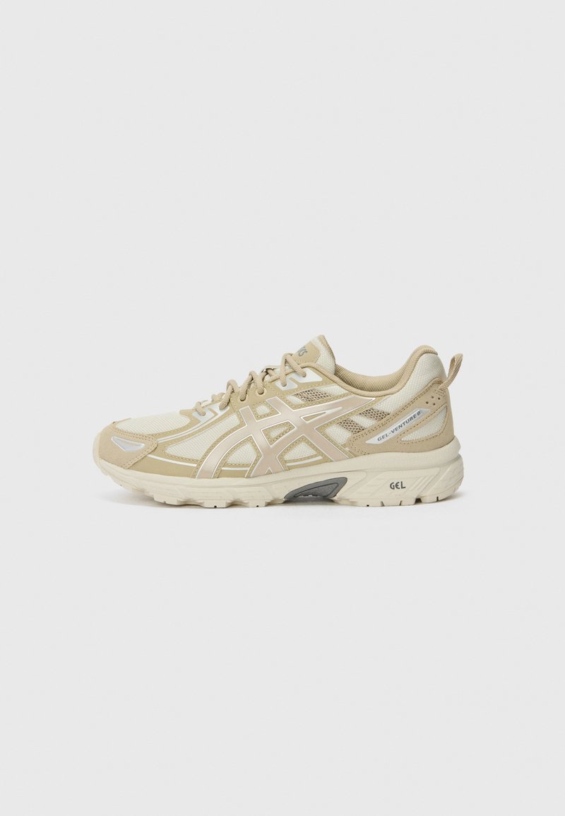 Beige running shoes with mesh and synthetic material, featuring a cushioned sole, distinctive logo detail, and a structured design.