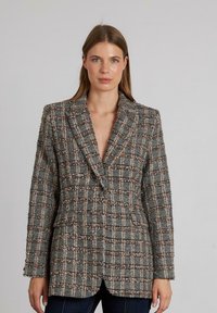 Blazer tejido en gris, blanco y marrón con patrón de cuadros. Cuenta con un ajuste entallado, solapas tipo pico y dos bolsillos delanteros. Tejido texturizado.