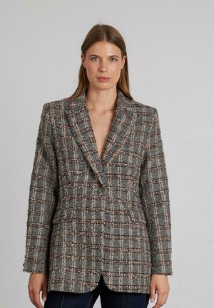 Blazer tejido en gris, blanco y marrón con patrón de cuadros. Cuenta con un ajuste entallado, solapas tipo pico y dos bolsillos delanteros. Tejido texturizado.