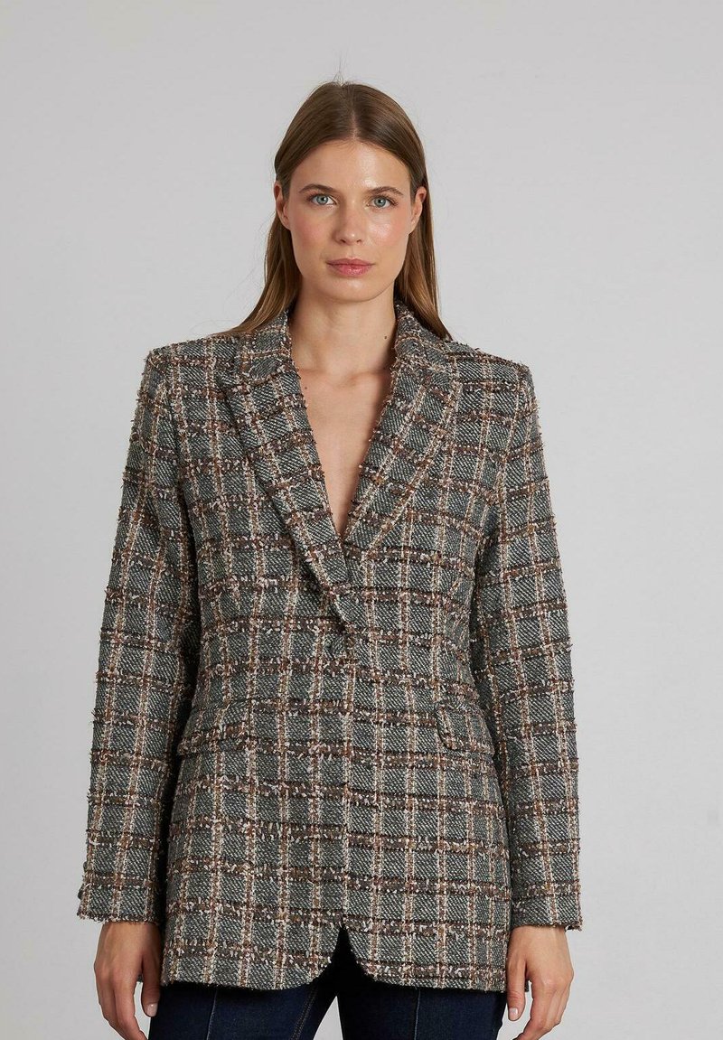 Blazer tejido en gris, blanco y marrón con patrón de cuadros. Cuenta con un ajuste entallado, solapas tipo pico y dos bolsillos delanteros. Tejido texturizado.