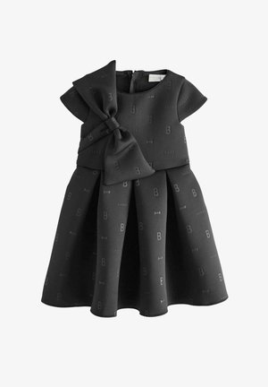 Vestido negro de tela texturizada, con detalle de lazo en la cintura, mangas cortas y falda plisada con patrones y logotipos en relieve.