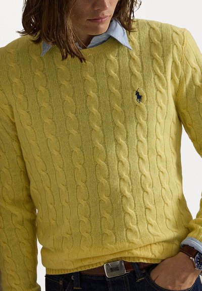 Dzeltenais adījuma džemperis, izgatavots no mīkstas, faktūras auduma, ar ribotām piedurknēm un apakšmalu, kā arī ar mazu tumši zilā krāsā esošu logotipa akcentu uz krūtīm.