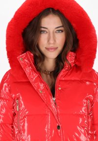 Czerwona błyszcząca kurtka puchowa z kapturem wyłożonym sztucznym futrem, dwoma bocznymi kieszeniami na zamek oraz złotymi dodatkami, z pikowanymi detalami.
