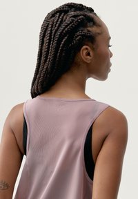 Bezrękawnik sportowy w jasnoróżowym kolorze z siateczkowego materiału. Posiada okrągły dekolt oraz kontrastową czarną podszewkę, charakteryzuje się gładką teksturą i oddychającym designem.