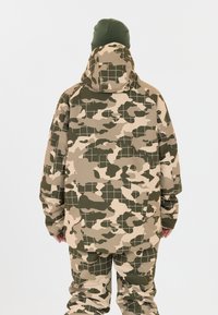 Camouflagejakke og bukser i nuancer af grøn og beige med et rutemønster. Hætte-design med en afslappet pasform og lange ærmer.