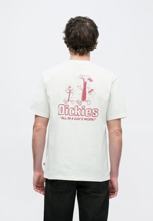 Katoenen T-shirt in off-white met een rode afbeelding op de achterkant met cartoonfiguren en de tekst "Dickies 'ALL IN A DAY'S WORK!'".