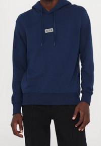 Marineblauer Hoodie aus weichem Stoff mit einer Kängurutasche vorne, Kapuze mit Kordelzug und einem kleinen Logopatch auf der Brust.