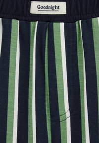 Bombažne kratke hlače za spanje z oznako na pasu, ki pravi "Lahko noč." Imajo navpične proge v mornarsko modri, zeleni in beli barvi ter stranski žep.