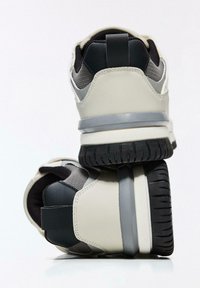 Két tónusú szürke és fekete kivitelű sportcipők, bőr és hálós anyagokból, lekerekített formával, texturált talppal és kontrasztos részletekkel.