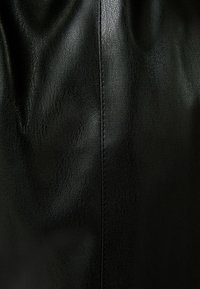 Cuero negro texturizado con un leve brillo, con costuras visibles a lo largo de la costura. El material presenta un patrón granular y un suave caído.