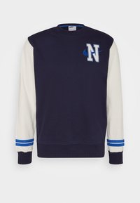 Navy blue sweatshirt with cream-colored sleeves, featuring an embroidered "N" logo and blue stripe accents on the cuffs.