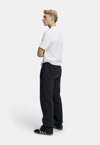 Vit kortärmad t-shirt, svarta sweatpants med sidofickor, enfaldig design, stående pose, lateral vy, accentuerad av svarta sneakers.