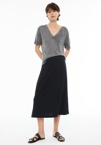 Top de punto gris de manga corta con escote en V y acentos de canalé, combinado con una falda larga negra y sandalias negras de tiras. Sencillo y monocromático.