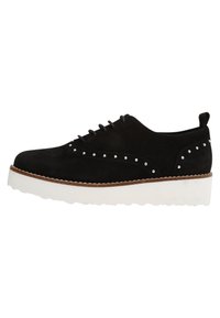 Zapato negro de ante con cordones, adornos de tachuelas plateadas, suela de plataforma blanca en contraste y diseño de punta redonda. Detalles laterales cóncavos.