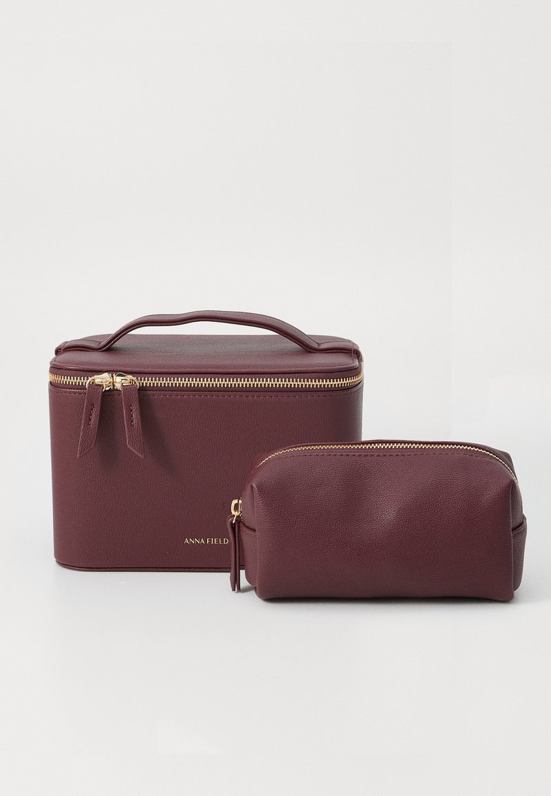 Burgundy faux leather cosmetic case with top handle, double zipper closure, and gold hardware. Smaller matching pouch included. Smooth texture.