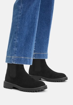 Czarne zamszowe botki Chelsea z elastycznymi bocznymi panelami i wytrzymałą gumową podeszwą, zestawione z krótkimi niebieskimi jeansami.
