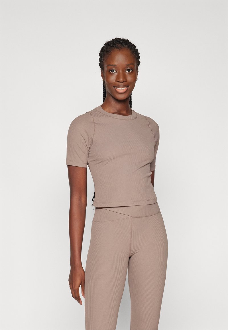 Top ajustado de manga corta en un material acanalado de color marrón claro, con un escote redondo y un diseño lateral sin costuras. Combina con leggings de cintura alta.