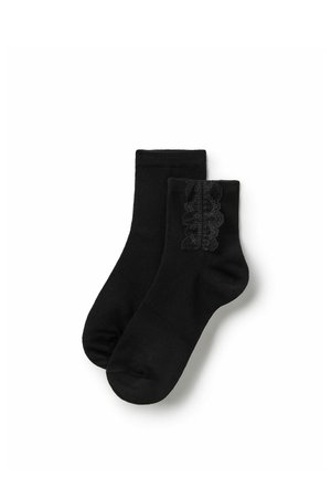 Paire de chaussettes noires à la cheville, dont une avec un détail volanté en dentelle sur le côté, présentée sur fond blanc.
